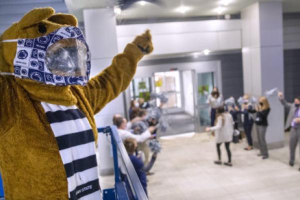 宾夕法尼亚州立大学的尼塔尼狮子站在前景，当一个人走过门口时，几个人在后面欢呼。