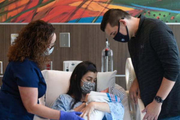 在医院病房里，一对新父母对着他们的新生儿微笑，医护人员则在一旁看着。