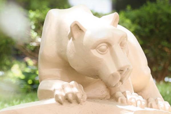 这是一尊雕像，描绘的是宾夕法尼亚州立大学的吉祥物，Nittany Lion，被灌木丛包围着。