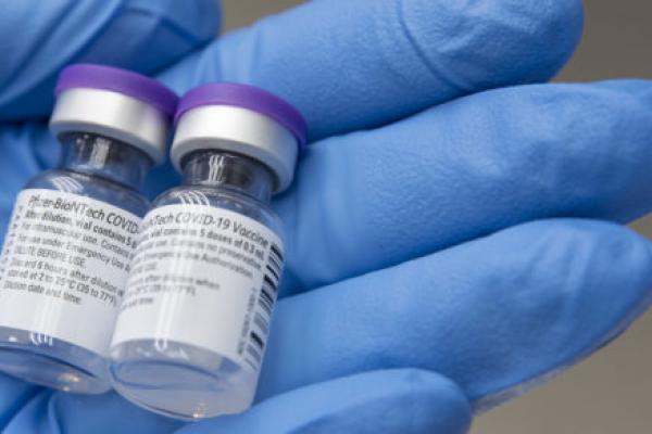 一个戴着手套的手抱着两瓶辉瑞生物技术公司新冠病毒-19疫苗的特写镜头。