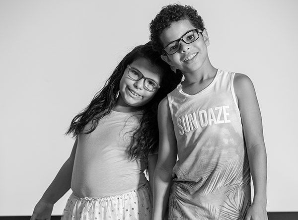 Gabriella Asadi靠在她哥哥的肩膀上Xavier。她有长发，穿着舞裙和顶部。Xavier有短卷发，戴上罐子上衣。在去年夏天，他们戴着眼镜，他们通过愿景来学习移动眼科诊所。