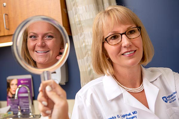 Doctor Lighthall is holding a hand mirror up to show the patient’s face during an examination.