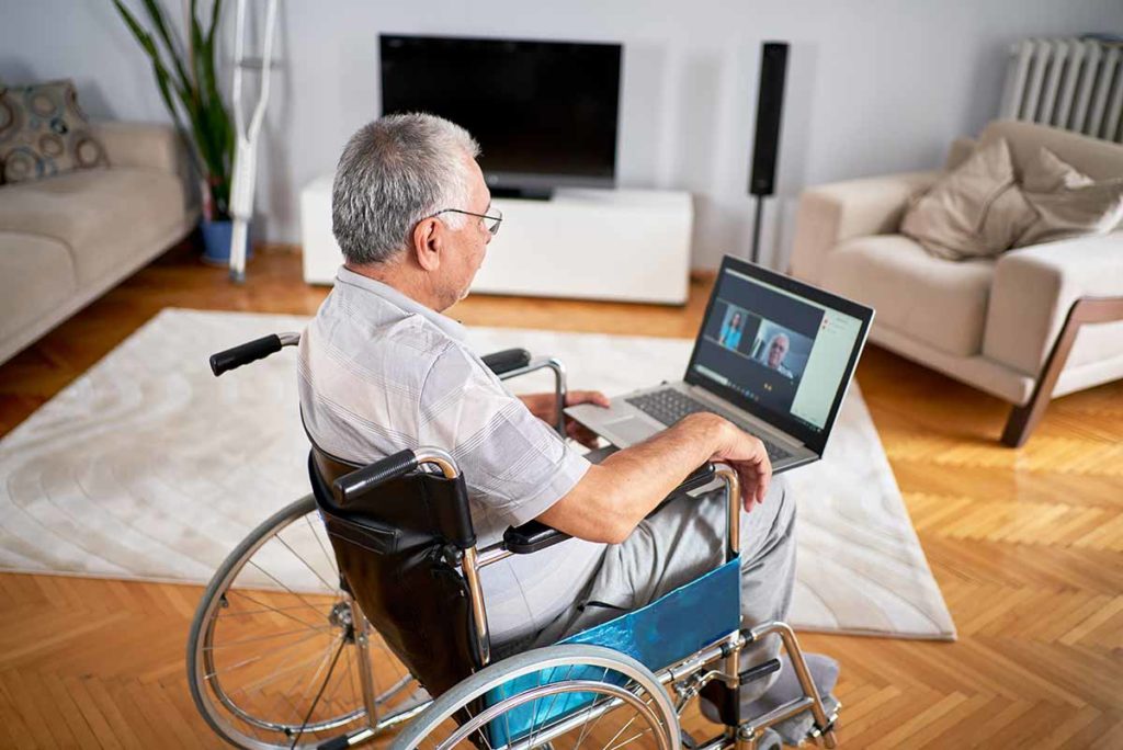 Older man sitting in wheelchair using laptop.