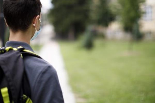 学校十几岁的男孩背面图有面孔防护面具的在学校前面。