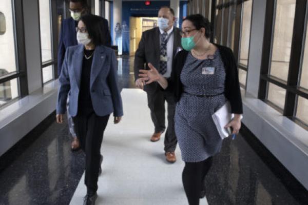 Four people – two women followed by two men – walk down a hallway with signage that reads “Penn State College of Medicine” and “Institute for Personalized Medicine.” As they walk, they look to their right, out of a set of windows.