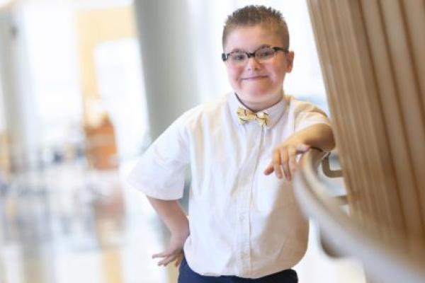 Gannon Kupko Jr. poses for a photo while leaning against a railing. Windows are in the background.