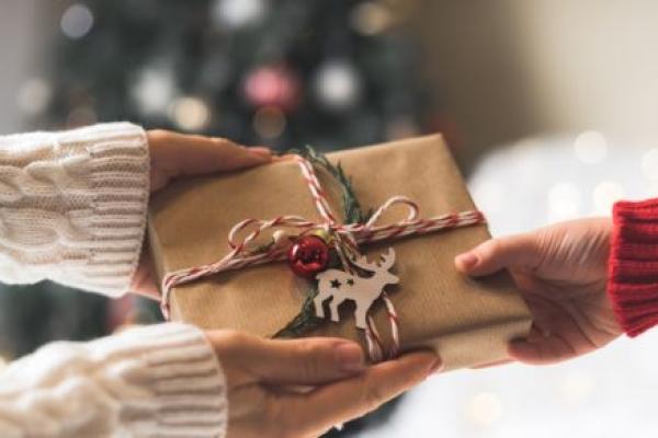Woman in sweater giving a wrapped Christmas gift box to child.