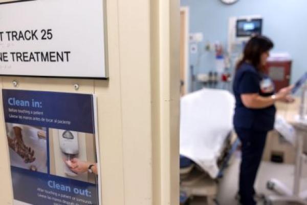 A nurse is seen out of focus on the right in the Sexual Assault Nurse Examiner room at Penn State Health St. Joseph Medical Center, A sign on the left reads: “Fast Track 25, SANE Treatment.” Another sign reads: “Clean in, Clean out.”