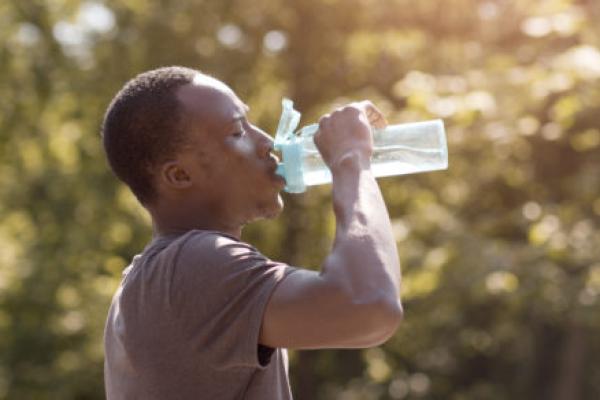 A thirsty man in the sun drinks a bottle of water.