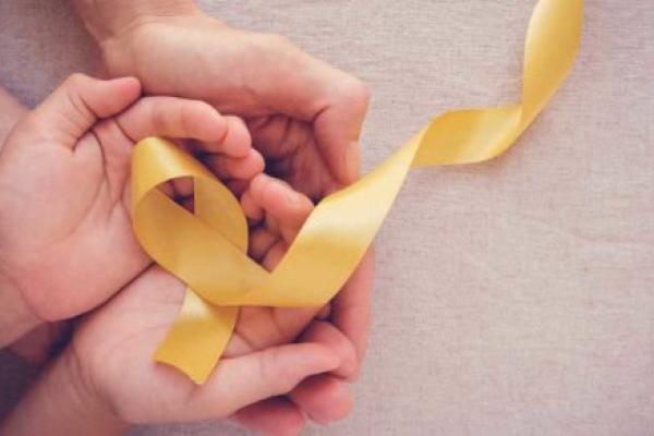 Image result of adult and child hands holding a yellow ribbon to represent childhood cancer awareness.